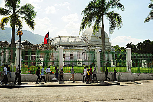 haiti,port,au,prince,champs,de,mars,camp,young,adults,walking,in,front,of,destroyed,presidential,palace