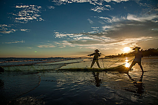 广西东兴京族万尾岛金滩渔民在晚霞中拖网捕鱼