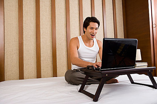一个男人坐在床上玩电脑