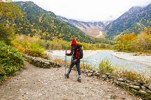 一个手拿登山杖在秋天的山谷河边徒步的女性徒步旅行者