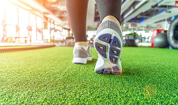 健身房一个女生穿着运动鞋,踩着草地,走向运动器械