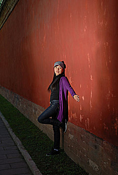 一名年轻女性背靠古老的红墙