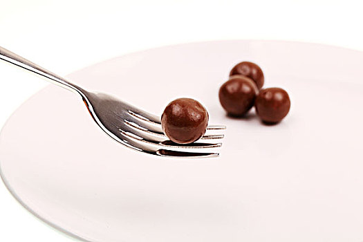 白色盘子中的四个圆形棕色巧克力豆和银色叉子