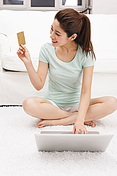 年轻女士坐在电脑旁拿着信用卡