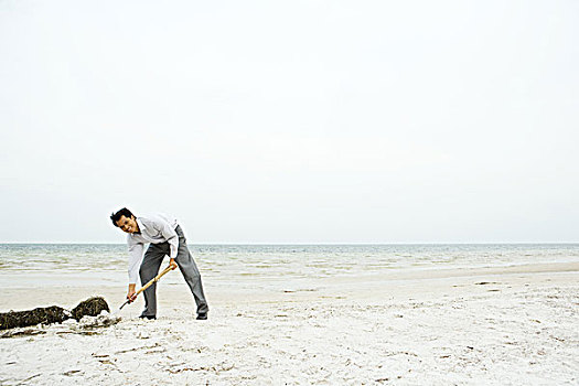 男人,海滩,弯腰,挖,沙子,看镜头,微笑