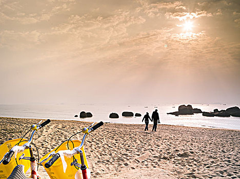 情侣手牵手迎着夕阳走在海边的沙滩上