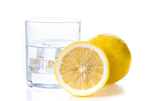 一个新鲜的切开的柠檬摆放在一个盛有冰块的玻璃水杯旁边