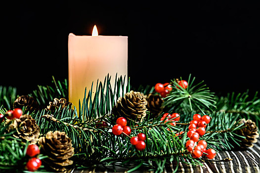 摆放在木质桌面上的圣诞树,红浆果和燃烧中的白色蜡烛