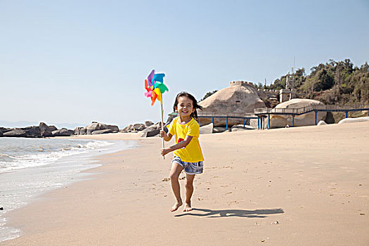 小女孩拿着风车在沙滩上奔跑