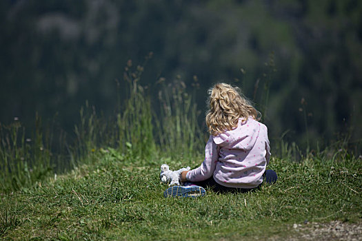 坐在山坡草坪上的西方金发小女孩