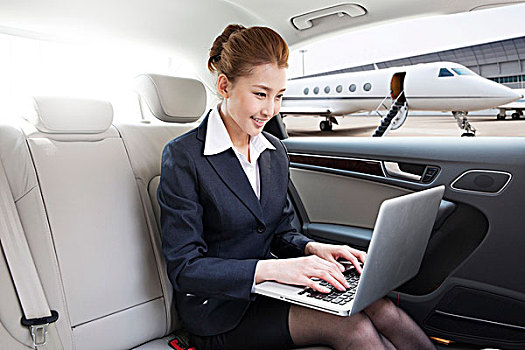 商务女士坐在轿车里使用笔记本电脑
