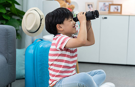快乐的小男孩拿着望远镜坐在行李箱上