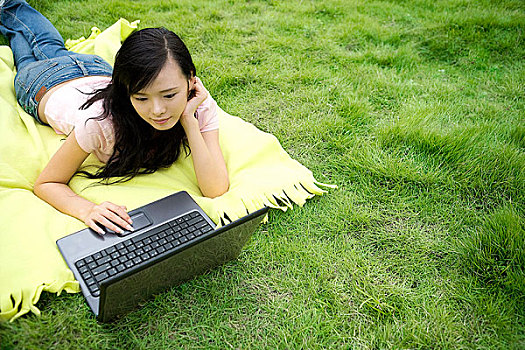趴在草地上拿着电脑的女孩