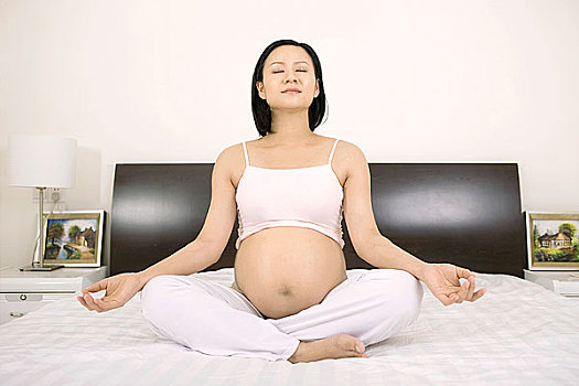 盘腿坐在床上练瑜伽的孕妇