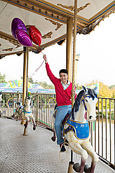 年轻男人在游乐园骑旋转木马