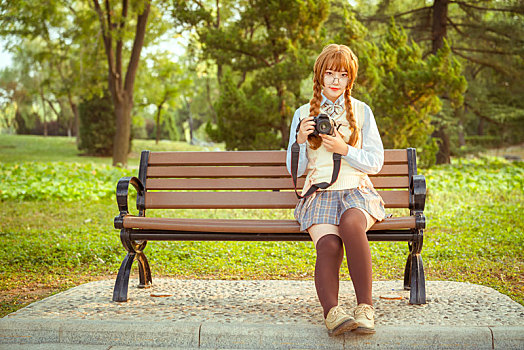 拿着相机的少女坐在公园长椅上