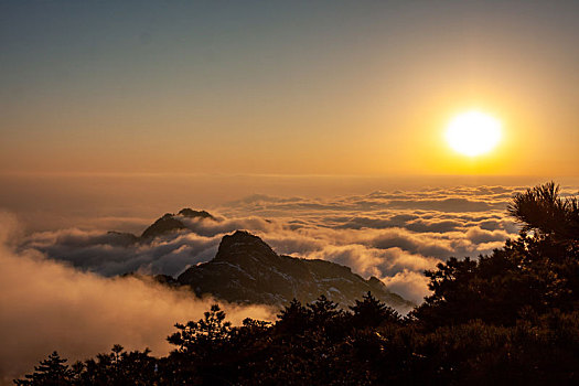 中国安徽黄山风景区,冬日雪后放晴,夕阳映照山崖云雾飘渺宛若仙境