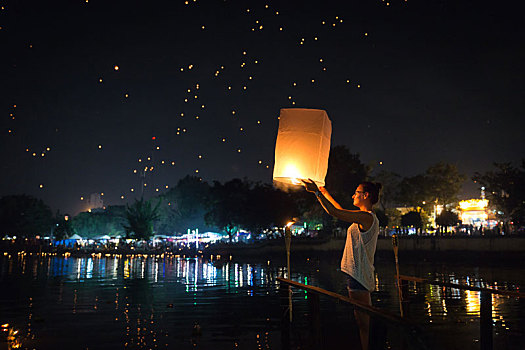 泰国清迈水灯节期间,一名西方女性在清迈湄平河边手持孔明灯正准备放飞