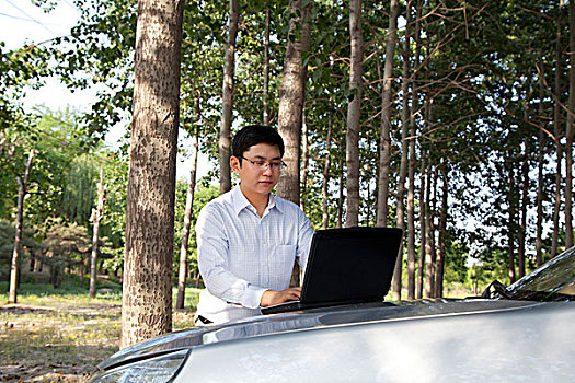 成功商务男士在汽车发动机盖上使用笔记本电脑