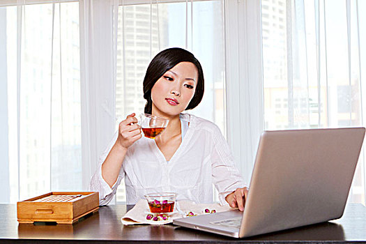 东方年轻女性喝茶和使用笔记本电脑