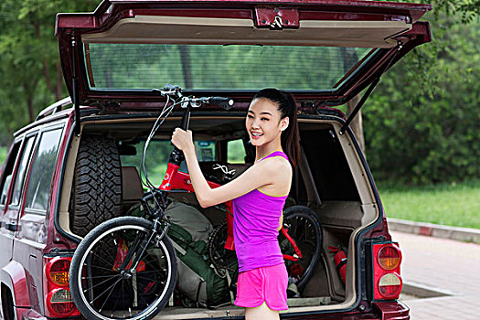青年女性把自行车放到汽车后备箱里