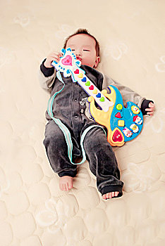 躺在床上玩吉他玩具的男婴