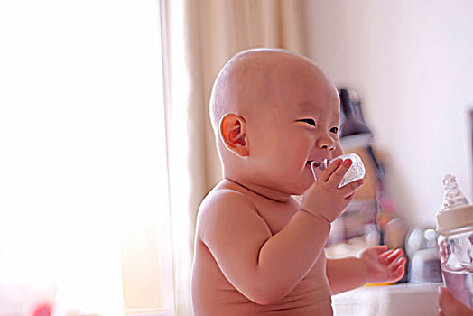 叼着奶瓶盖在玩的婴儿