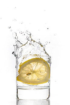 一片新鲜的柠檬片掉入玻璃水杯中的瞬间水花飞溅空中
