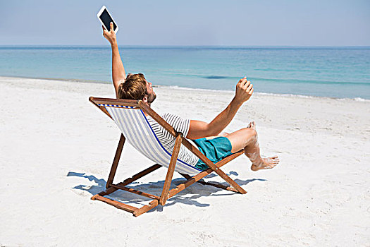 男人,伸展胳膊,拿着,数码,坐,折叠躺椅,海滩