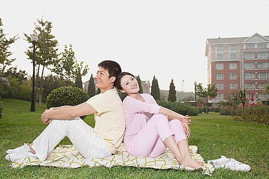 年轻情侣背靠背坐在草地上