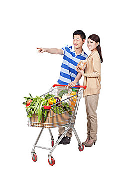 一对青年男女手拿面包和一辆装满蔬菜的购物车