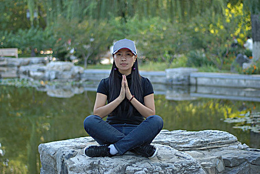 一名年轻女性坐在河岸边的巨石上打坐