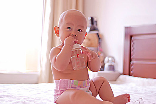 一名八个月的女婴在床上喝水