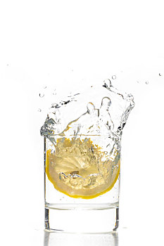 一片新鲜的柠檬片掉入玻璃水杯中的瞬间,水花正要从杯里飞溅而出