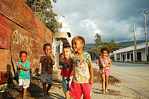 group,of,timorese,children,with,thumbs,up,in,the,street,under,dark,clouds