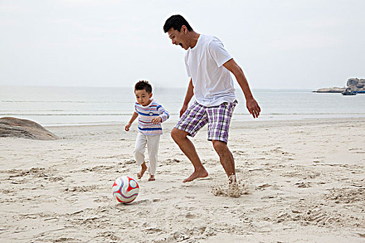 中年人和小男孩在海边踢足球