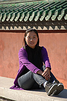 一名年轻女性坐在古老的红墙前