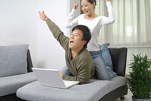 沙发上对着电脑坐在老公背上表情兴奋的年轻女人
