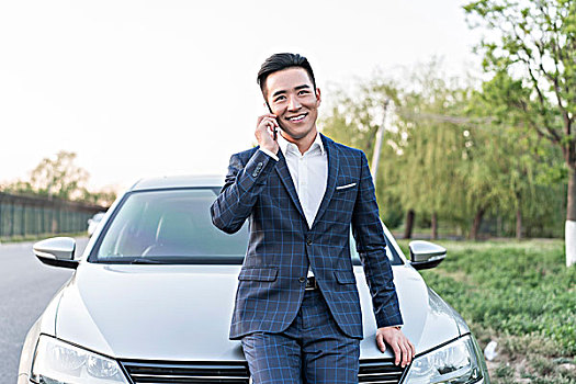 商務男士倚車而站打電話