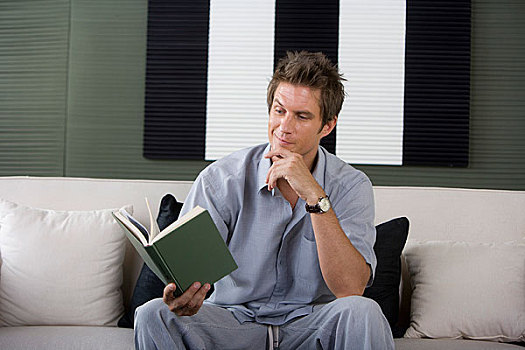 一个穿着休闲装的男人坐在沙发上看书