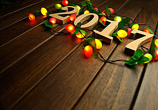 2017新年快乐,木质数字和闪烁的彩灯放在复古桌面上