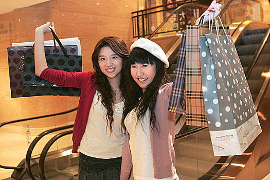 两个快乐的年轻女子举着购物袋