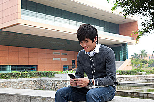 年轻男大学生在校园里使用笔记本电脑听音乐