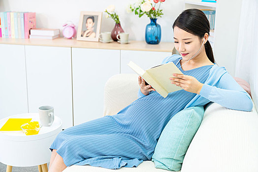 年輕孕婦在沙發(fā)上看書