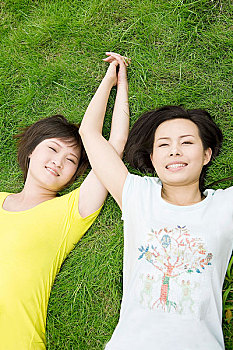 草地上手牵手躺着的两个女孩