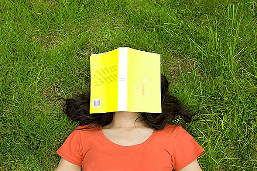 躺在草地上用书覆盖脸的女孩